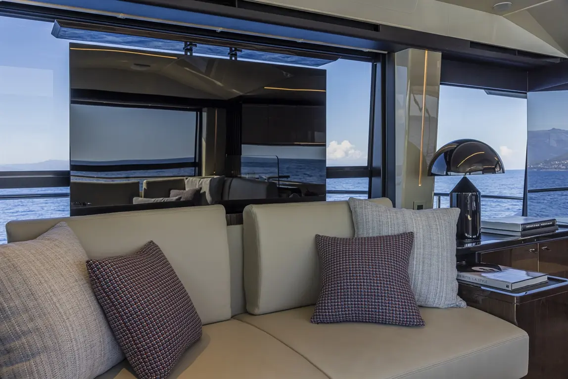 Interior of a luxury yacht lounge with a beige sofa, patterned cushions, and a view of the sea through large windows.